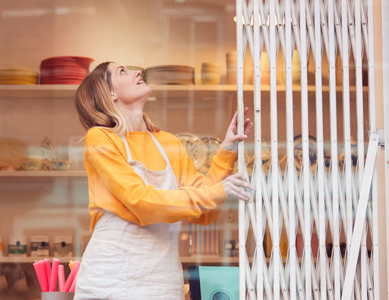 Mujer cerrando con una verja un local comercial