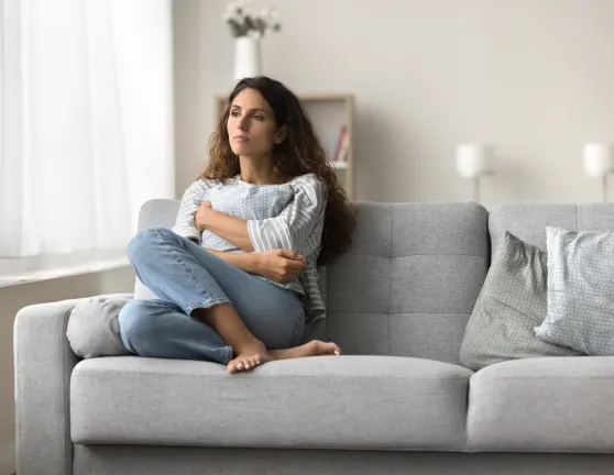 Mujer con expresión de tristeza sentada en el sofá de su casa